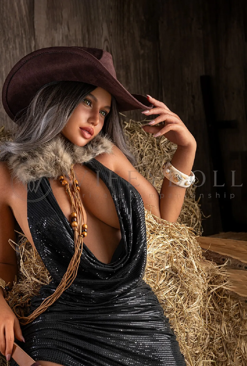 Celine sits beside the hay bales in a brown cowboy hat, fur collar, and black shimmer dress, lifting a hand toward the brim.