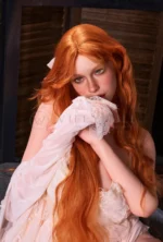 Darcy rests her lace-covered hand near her lips, framed by long copper-red waves.