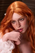 Darcy rests a finger near her lips, revealing amber eyes and freckles between copper-red waves.