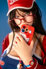 Face close-up of Hanae, a 161cm realistic companion doll, wearing red glasses with a red phone held near her mouth.