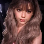 Close-up of Livia with soft brown eyes, straight bangs, and long ash-brown waves, a pink lingerie strap visible near one shoulder.