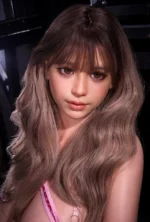 Close-up of Livia with soft brown eyes, straight bangs, and long ash-brown waves, a pink lingerie strap visible near one shoulder.