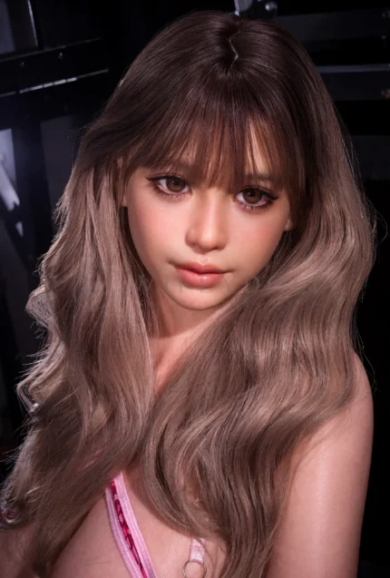 Close-up of Livia with soft brown eyes, straight bangs, and long ash-brown waves, a pink lingerie strap visible near one shoulder.