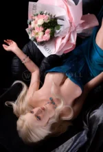 Lottie lies back comfortably in the chair, one arm relaxed away from her body as the bouquet rests above her shoulder and the teal corset stays fitted at the waist.