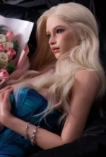 Lottie reclines beside the bouquet and looks upward to the side, one hand resting near the teal neckline as blonde waves fall over her shoulder.