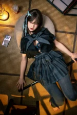 Mika, a 161cm realistic sex doll, reclining on a round cushion in a pleated skirt and gray stockings, one leg bent.