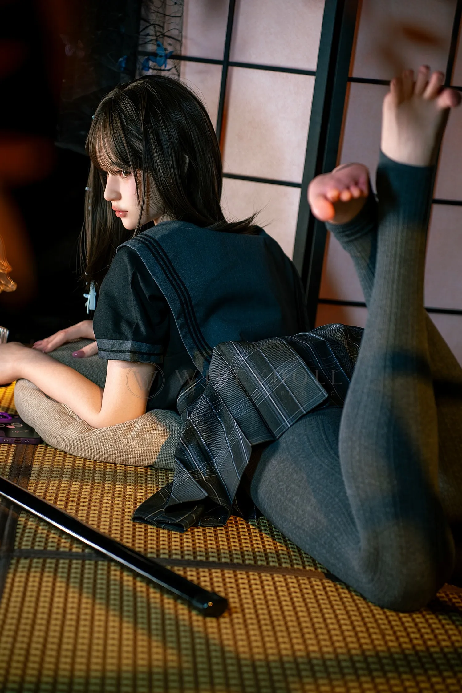 Mika, a 161cm silicone companion doll, lying face down from the rear side, with both stockinged legs bent behind the pleated skirt.