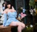 Mina silicone companion doll seated on a wooden bench with flowers behind her.