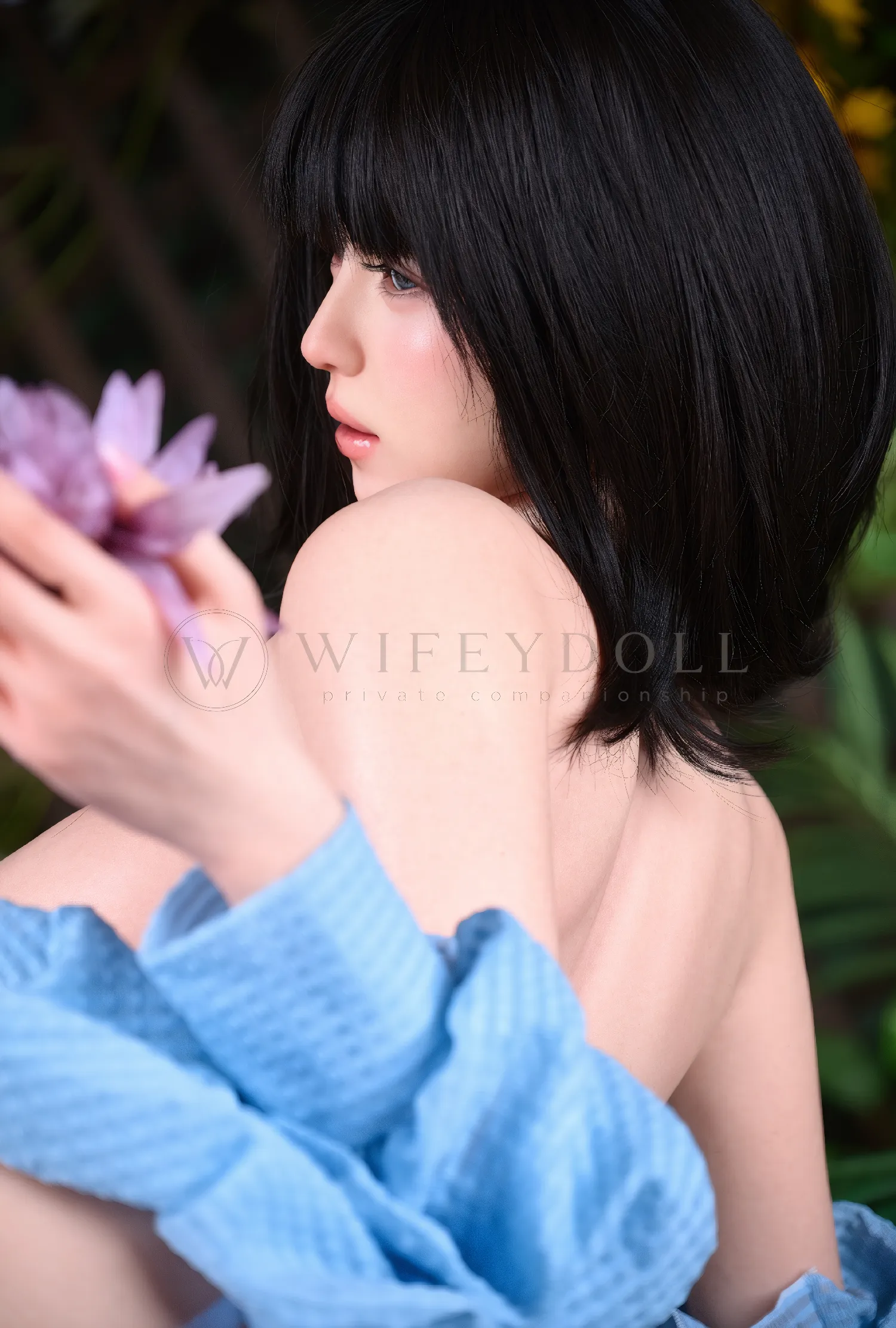 Mina Asian silicone doll seated sideways beside a cluster of pink flowers.