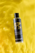 An upright bottle of Slip Me In lubricant stands amid rippling water on a yellow background.