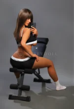 Victoria, a 168cm realistic love doll, turns sideways on the bench as long dark hair falls down her back.