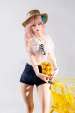 Mio, a 166cm life-size silicone doll, stands beside a yellow shopping cart while holding a small basket of oranges.