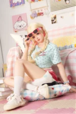 Xia Ying silicone doll reclining near pastel cushions, one leg raised on the bed.