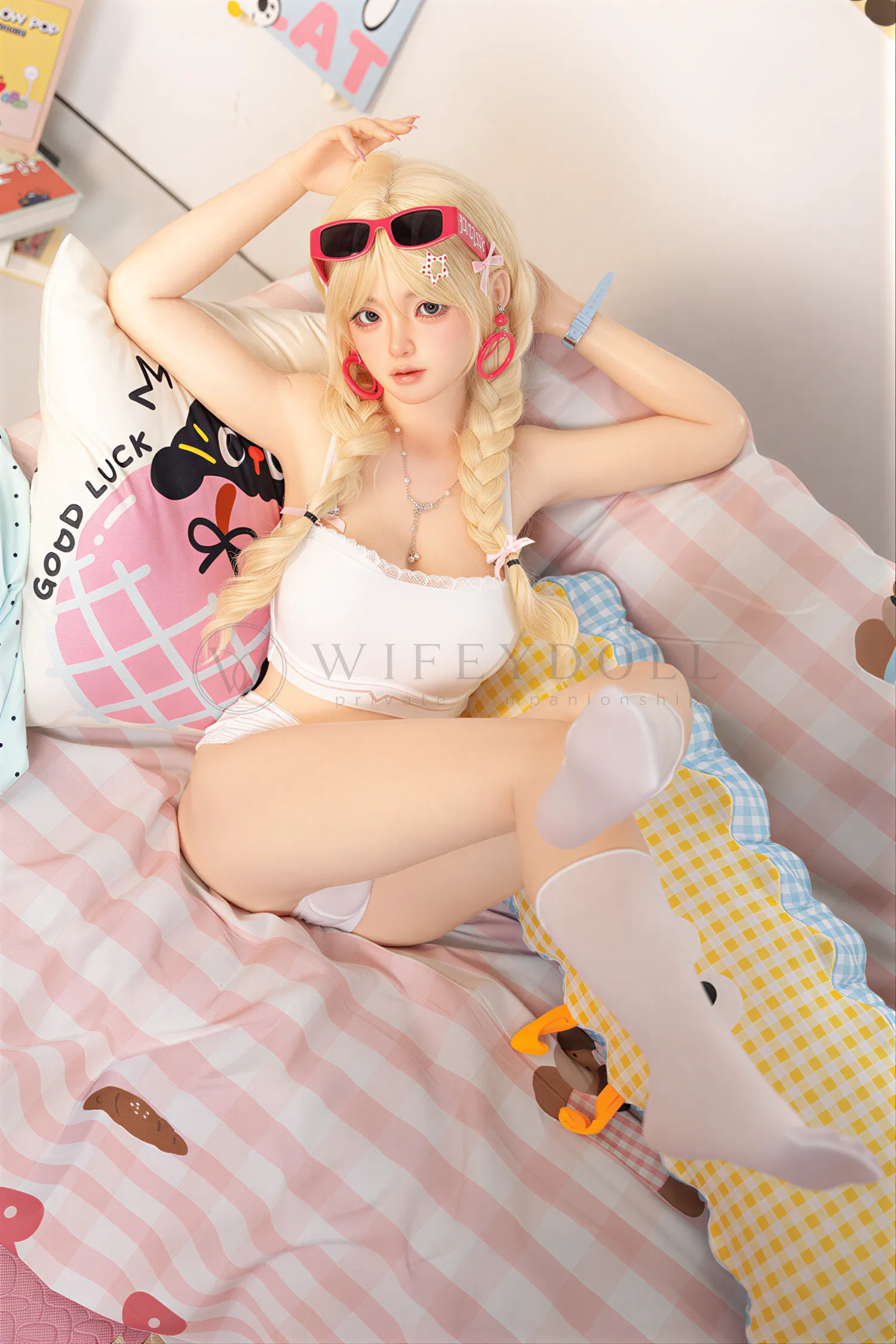 Xia Ying silicone doll seated on the bed in a white top, raising both hands near her head.