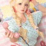 Xia Ying silicone companion doll seated on the bed, holding a pink phone handset and reaching one hand forward.