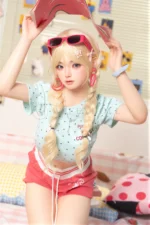 Xia Ying silicone doll seated on the bed, lifting a pink box above her head.