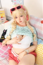 Xia Ying silicone doll seated on the bed in a white top, one hand resting over her chest.