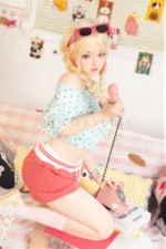 Xia Ying silicone doll kneeling on the bed, one hand resting near her knee.