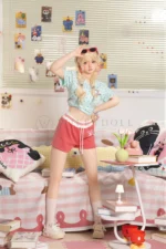 Xia Ying 148cm petite silicone sex doll standing in a pastel bedroom in a mint top and red shorts.