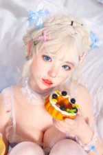 Zia, a 154cm realistic companion doll, holds a fruit tart beside her face, with blue eyes and pastel clips in her blonde braids.