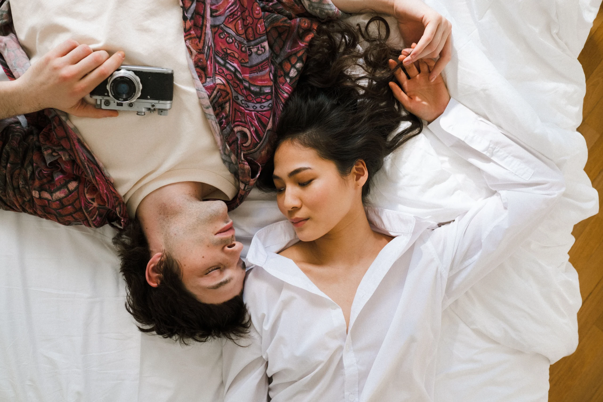 A couple lying close together on white bedding.