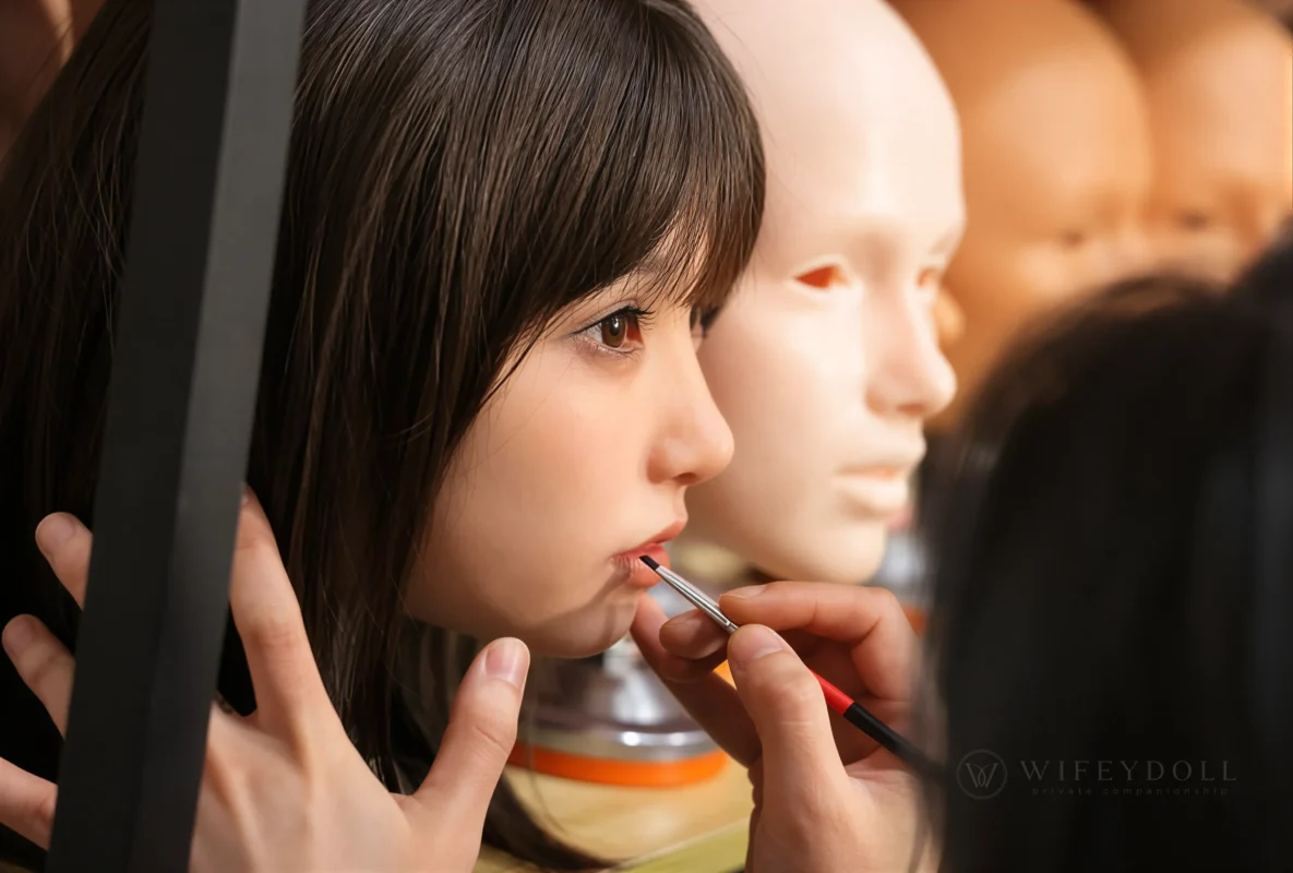 Technician applying makeup to a custom silicone doll head in the workshop.
