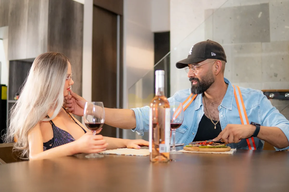 A man sitting beside a companion doll at the dinner table, gently touching her chin.