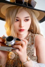 Vivienne realistic silicone sex doll facing forward in a straw hat, holding a camera over her floral-trimmed top.
